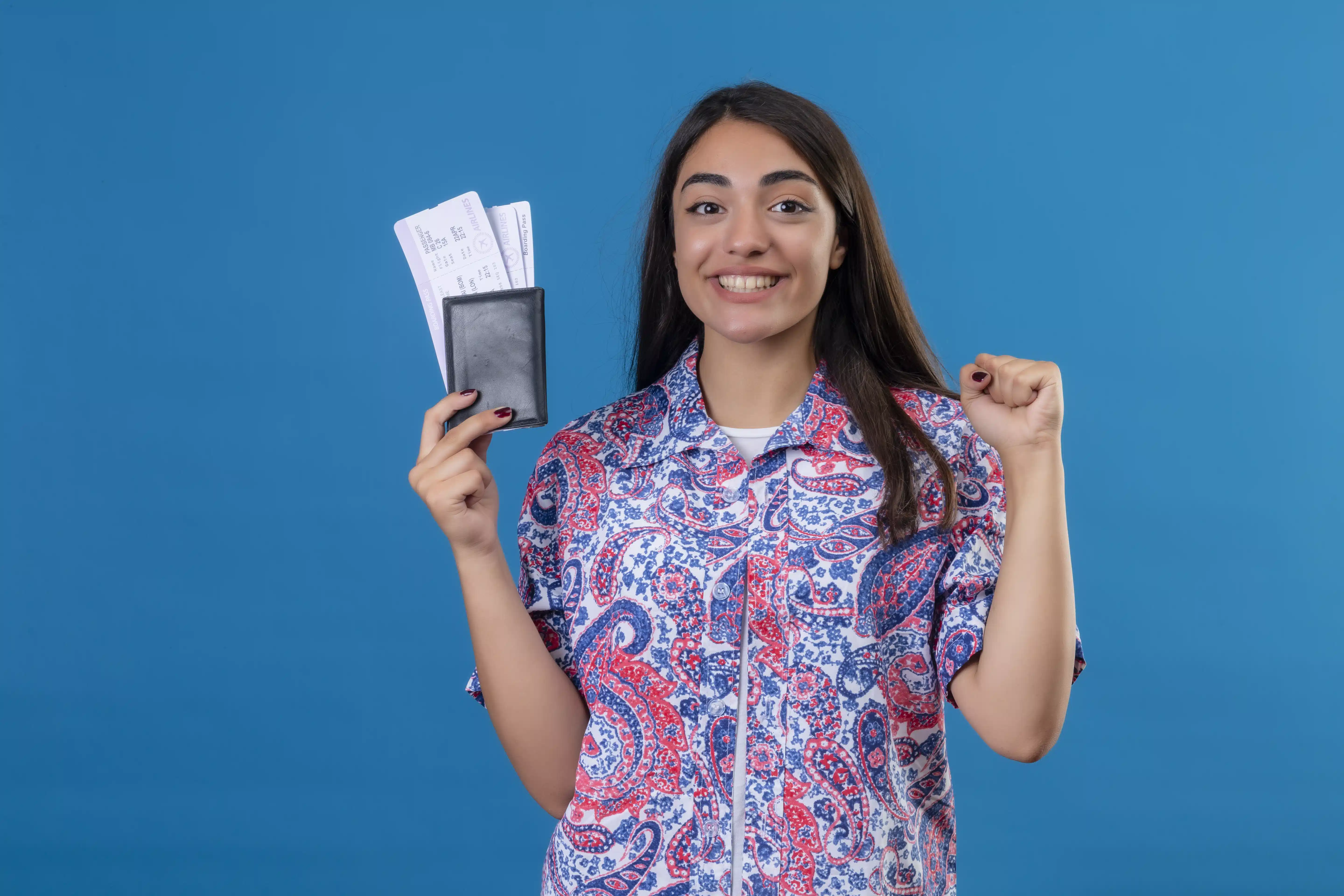 young-beautiful-traveler-woman-holding-passport-with-tickets-smiling-cheerfully-raising-fist-after-victory-ready-holiday-isolated-blue-wall